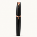 Black electric eyebrow trimmer with rose-gold accents on a warm white background